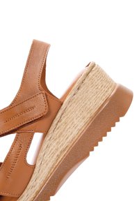 Sandal in pelle marrone con suola platform. Presenta un tacco testurizzato e ritagli laterali. Cinghie in velcro per la regolazione.