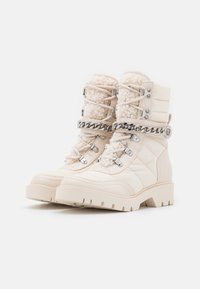 Stivali da trekking beige trapuntati con colletto in finta pelliccia, dettagli in catena argentata e suole in gomma robuste. Presentano anelli metallici e chiusure con lacci.