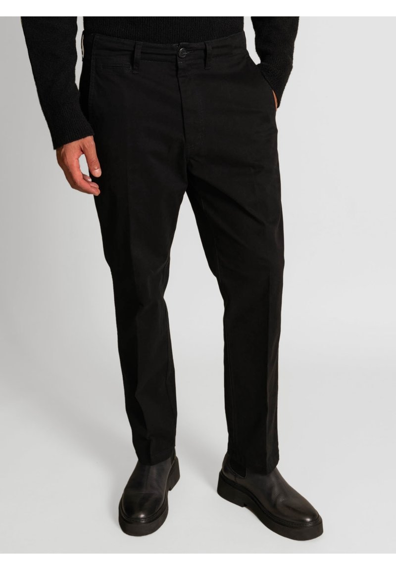 Black trousers made of cotton blend, featuring a straight fit, front pockets, and a single button closure. Worn with black ankle boots.