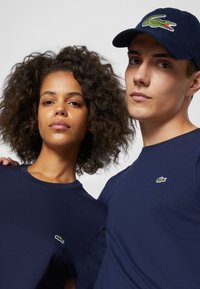 Marineblauwe t-shirts met ronde halslijnen, voorzien van kleine geborduurde Lacoste krokodillenlogo's op de borst.