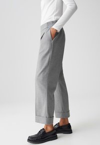 Grijze getextureerde broeken met een elastische tailleband en opgerolde hemden, gecombineerd met zwarte schoenen met een decoratieve rand.