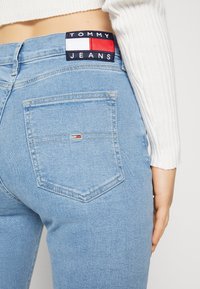 Jeans de mezclilla azul claro con un ajuste de cintura media, que cuentan con un bolsillo trasero con un pequeño parche de logo y una etiqueta en la cinturilla de contraste.