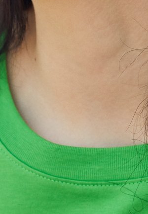 Neck and lower face area with dark hair strands, wearing a bright green crew-neck shirt.