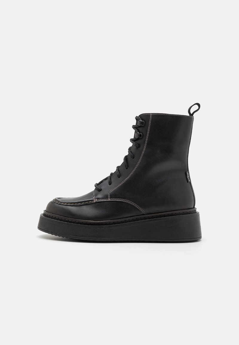 Bottes basses en cuir noir avec semelle plateforme, design à lacets, détails de couture et une languette à la cheville pour un enfilage facile.