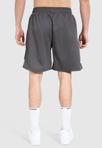 Pantalones cortos deportivos grises hechos de un tejido ligero. Cuentan con una cinturilla elástica, un ajuste holgado y una textura suave. Se llevan con calcetines blancos y zapatillas.