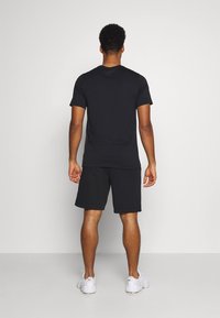 Svart kortärmad t-shirt i kombination med svarta shorts, båda i lätt material. Modellen ses bakifrån och bär vita sneakers.