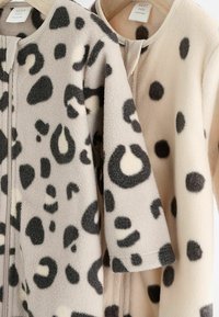 Zwei Fleecejacken hängen zusammen, eine in Beige mit schwarzen Flecken und die andere in Grau mit schwarzen und cremefarbenen, leopardähnlichen Mustern.