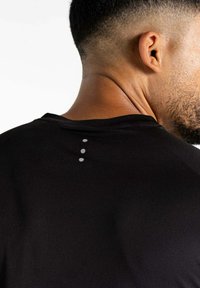 Schwarzes Sportshirt mit rundem Ausschnitt, strukturiertem Stoff und drei kleinen grauen Punkten auf der Rückseite als Designdetail.