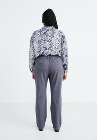 Mönstrad blus med ormskinnstryck i svart, vitt och grått, kombinerad med grå, avslappnade byxor med elastisk midja och fickor.