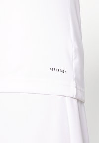 Acercamiento de ropa atlética blanca mostrando el logo "AEROREADY" cerca del dobladillo inferior en una tela suave y ligera.
