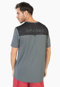 Lyhythihainen miesten t-paita harmaasta kankaasta, jossa on musta kamouflagekuviointi ylhäällä ja "SPYDER"-logo takana. Paita on rentoa mitoitusta.