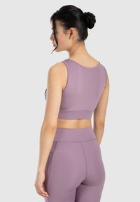Sujetador deportivo morado con un diseño sin costuras, escote redondeado y estilo de espalda de nadadora ajustado. Tela suave y elástica con una textura lisa.