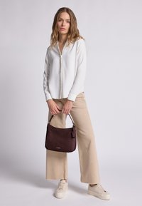 Blusa chiara con colletto, pantaloni beige a gamba larga, sneakers color crema e una borsa bordeaux testurizzata con tracolla corta.