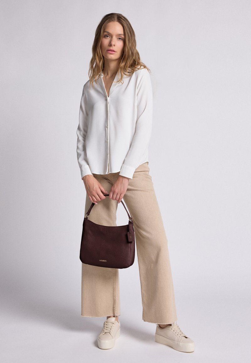 Blusa chiara con colletto, pantaloni beige a gamba larga, sneakers color crema e una borsa bordeaux testurizzata con tracolla corta.