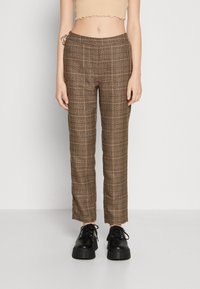 Pantalon marron à carreaux avec une coupe ajustée, doté d'une taille taille mi-haute et d'une texture lisse. Associé à des chaussures plateformes noires.