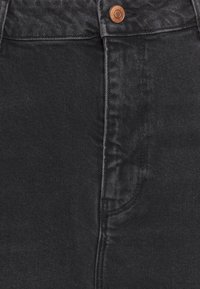 Schwarze Denim-Jeans mit schmal zulaufendem Schnitt, Kupferknopf-Detail und diagonaler Taschennaht. Strukturierter Stoff mit glatter Oberfläche.
