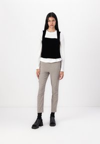 Černý sametový top na ramínka přes bílou košili s dlouhým rukávem, doplněný o kostkované slim-fit kalhoty a robustní černé sandály na podpatku.