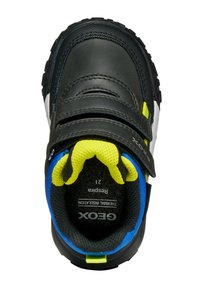 Zapatilla negra con correas de velcro, con acentos amarillos y azules. Parte superior texturizada con suela duradera. Etiqueta de tamaño 21 en el interior.