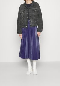 Svart denimjacka med klassisk krage, två bröstfickor; lila plisserad kjol; vita klackboots ger en kontrasterande avslutning.