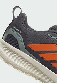 Wasserabweisender grauer Sneaker mit orangefarbenen Akzenten, strukturiertem Obermaterial und gerillter weißer Sohle. Mit einem Ziehdurch und seitlichen Belüftungsöffnungen.