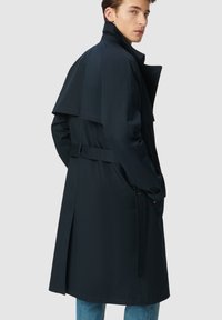 Granatowy trencz z podwójnym zapięciem, paskiem w talii, bocznymi kieszeniami i klasycznym kołnierzem, wykonany z gładkiego materiału.