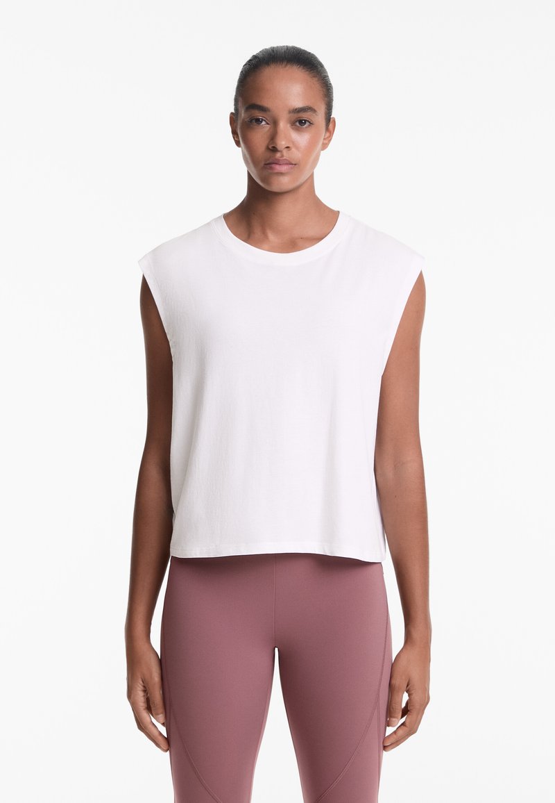 White sleeveless top with a round neckline, featuring a loose fit and soft texture, paired with high-waisted pink leggings.