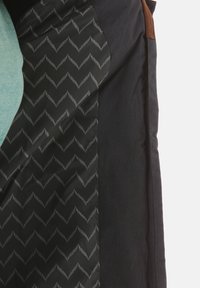 Bunda s kapucí s tyrkysově modrým předním dílem, černým vnitřkem s bílým vzorem ve tvaru šipky a hnědými koženými detaily. Hladká textura a moderní design.