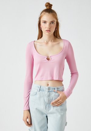 Vaaleanpunainen ribbed pitkähihaisuus crop toppi, jossa on pyöreä kaula-aukko ja ympyräleikattu keskiössä, yhdistettynä vaaleansinisiin korkeavyötäröisiin farkkuihin.