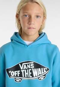 Modrá mikina s kapucí vyrobená z měkké látky, s černobílým logem „Vans“ a textem „OFF THE WALL“ na přední straně, se stahovací kapucí.