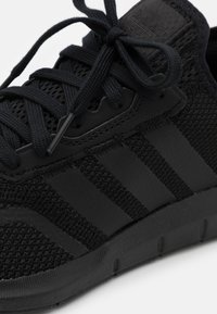 Baskets noires avec une tige en maille texturée, comportant trois stripes noires et des lacets noirs. La semelle est en caoutchouc avec une finition lisse.
