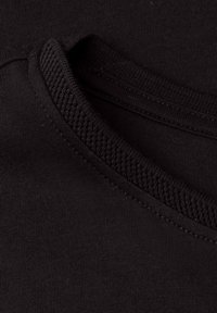 Gros plan d'un tissu noir montrant une couture texturée et côtelée du col sur un vêtement en tricot doux.