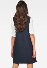 Marinblå A-linje klänning med en något texturerad finish, prydd med en kontrasterande vit skjorta under och en ren, enkel design.