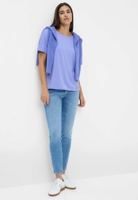 Lys lilla t-shirt med korte ærmer, lagdelt med en matchende cardigan. Sammen med lyseblå skinny jeans og hvide sneakers.