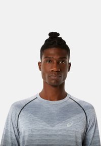 Grijze sport t-shirt met geometrisch patroon en effen kleurvlakken. Korte mouwen, ronde hals en reflecterend logo-detail op de borst.