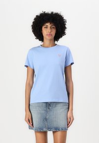 Tricou din bumbac de culoare bleu deschis, cu gât rotund și mâneci scurte, având un mic logo sub formă de triunghi roșu pe partea stângă a pieptului.