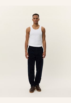 White tank top, dark blue corduroy pants with a straight fit, and brown lace-up shoes, standing against a neutral background.