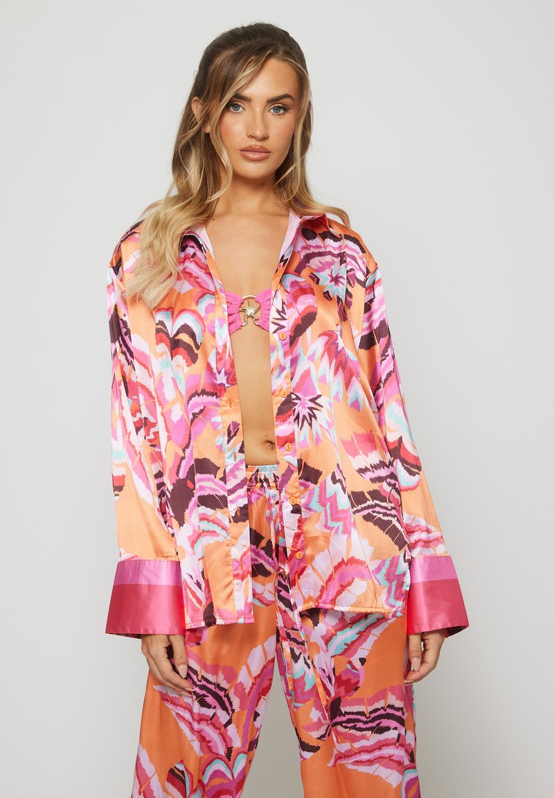 Conjunto de pijama de seda con un patrón abstracto en naranja y rosa. La camiseta tiene un cierre frontal de botones y puños anchos con un acabado brillante.