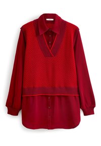 Rotes Langarm-Hemd mit Knopfleiste, kombiniert mit einem ärmellosen roten Strickwesten mit tiefem V-Ausschnitt und subtilen geometrischen Mustern.