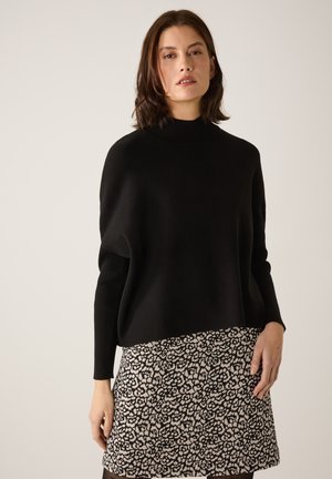 Schwarzer, oversize Pullover mit hohem geripptem Kragen, kombiniert mit einem gemusterten Kurzrock mit einem schwarz-cremefarbenen Blumenmuster.