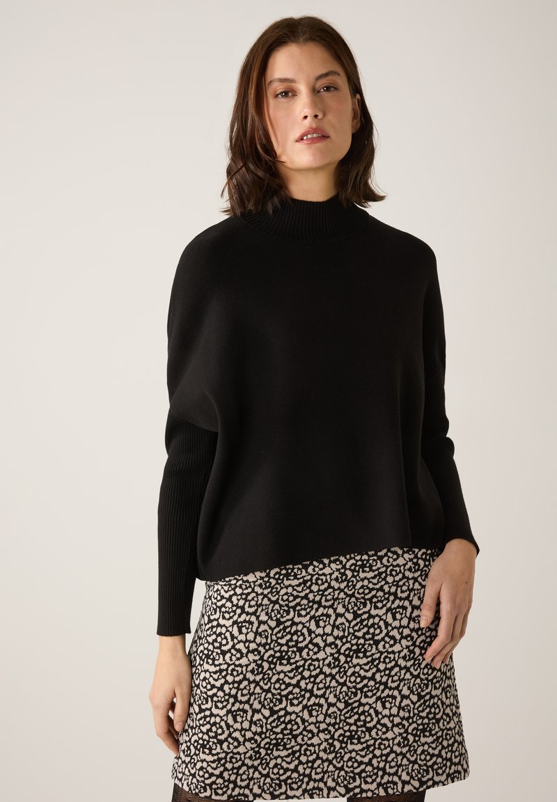 Schwarzer, oversize Pullover mit hohem geripptem Kragen, kombiniert mit einem gemusterten Kurzrock mit einem schwarz-cremefarbenen Blumenmuster.