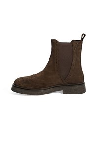 Bottines Chelsea en daim marron avec des panneaux élastiques, des détails de brogue le long des bords et une semelle en caoutchouc noir texturé. Hauteur de cheville basse.