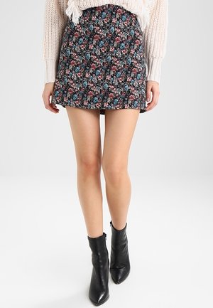Falda negra con diseño acampanado, decorada con flores rosas y azules sobre un fondo oscuro. Combinada con botas de tobillo negras de punta.