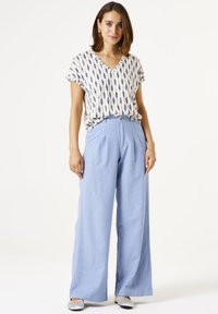 Leichtes, gemustertes V-Ausschnitt-Top in Creme und Marineblau, kombiniert mit blauen weiten Hosen mit hoher Taille und Vorderfalten. Silberne Ballerinas.