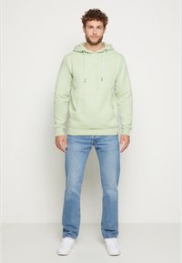 Lichtgroene hoodie met verstelbare trekkoorden, een voorkantzak en geribbelde manchetten, gecombineerd met een spijkerbroek in het blauw en witte sneakers.