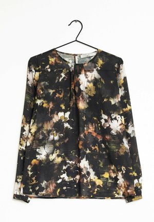 Blouse à manches longues avec imprimé floral abstrait noir, blanc, marron et jaune, col rond et découpe en goutte d'eau au dos, suspendue sur un cintre noir.