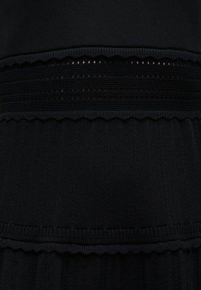 Tissu noir avec des motifs en maille texturée et des bandes horizontales comportant des bords festonnés et des détails en ajouré.