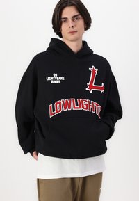 Black hooded sweatshirt with red embroidered "LOWLIGHT" and graphic "L." Features a relaxed fit and layered white shirt underneath.