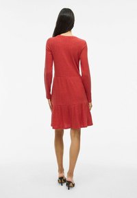 Rotes geripptes Kleid mit langen Ärmeln, einer taillierten Oberseite und einem ausgestellten, gestuften Rock. Hergestellt aus weichem Stoff, hat es eine subtile Textur.