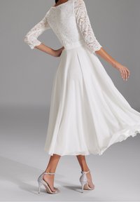 Vit klänning med spetsliv och trekvartslånga ärmar, flödande chiffongsärker och silverfärgade stilettklackar med ankelsnören.