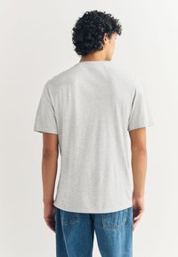 Camiseta de algodón gris de corte holgado, con mangas cortas y cuello redondo, combinada con jeans de mezclilla azul. Tejido texturizado y suave.